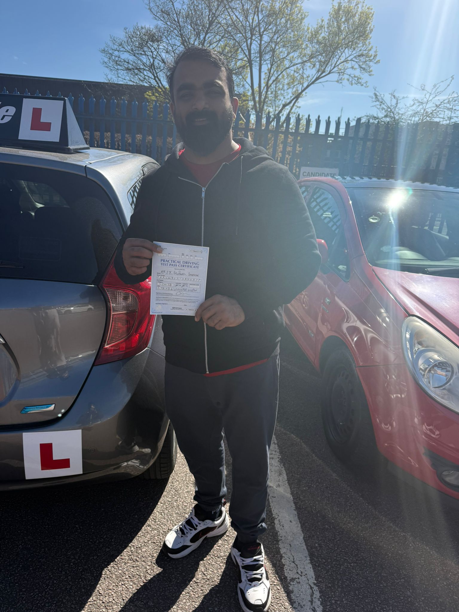 Successful Master Miles student holding driving test pass certificate beside learner car